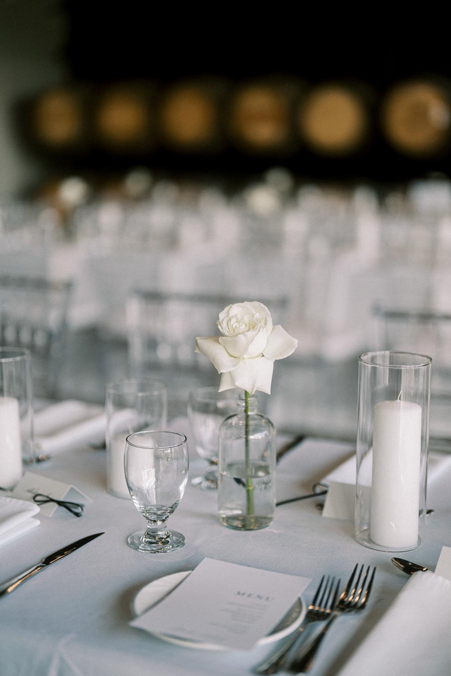 Elegant wedding table setting with a white rose centerpiece, crystal glassware, and a minimalist menu, creating a sophisticated ambiance for a formal event.