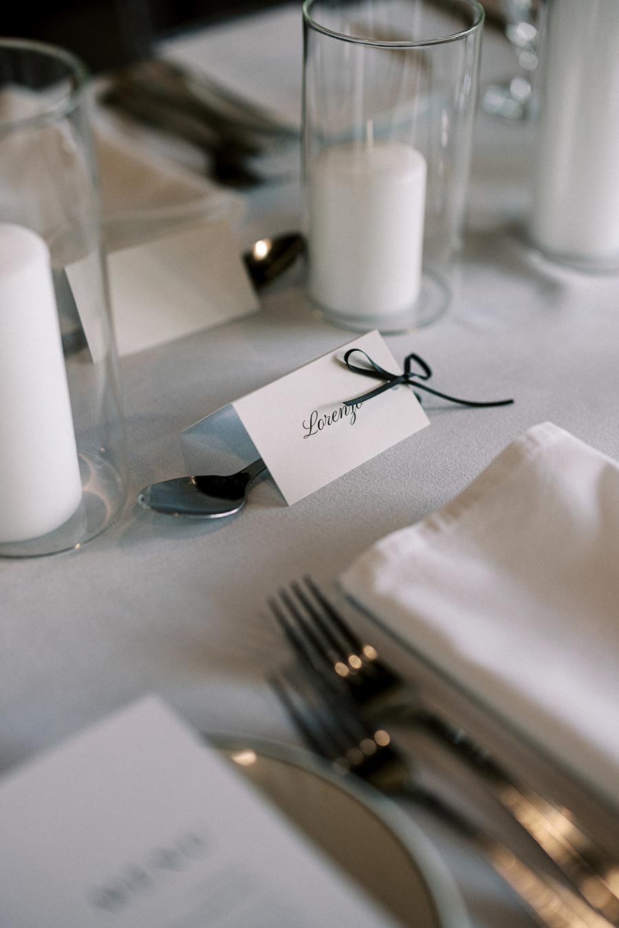 Elegant wedding table setting with a name card, candles, cutlery, and a white napkin on a neatly arranged dining table.