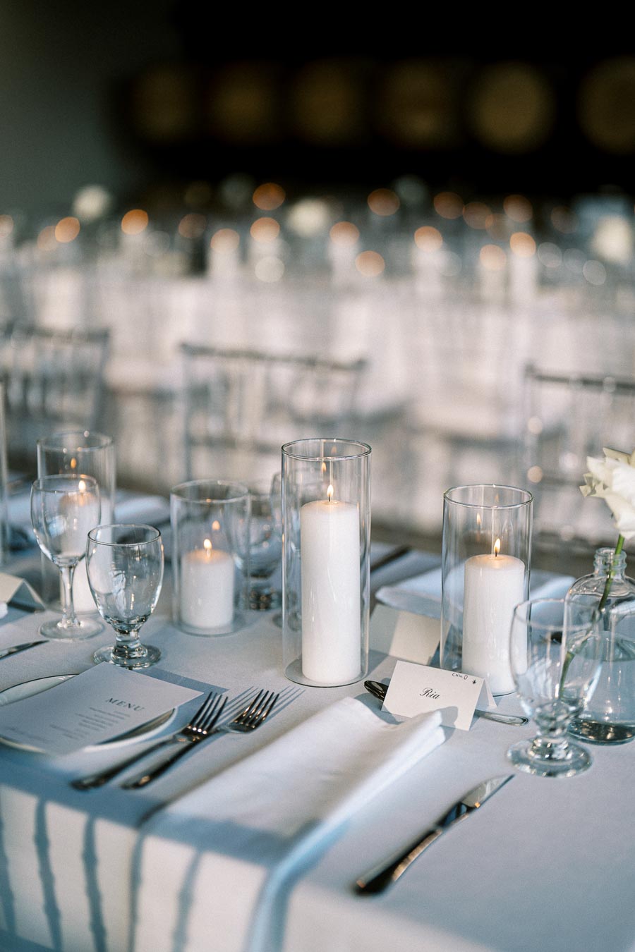 Elegant wedding table setting with white tablecloth, candles, glassware, and menus, creating a romantic atmosphere.