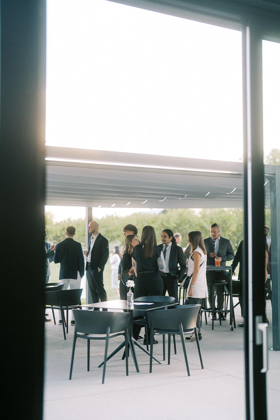 Group of people networking at an outdoor event in a modern patio setting with stylish black chairs and tables, under a bright open sky.