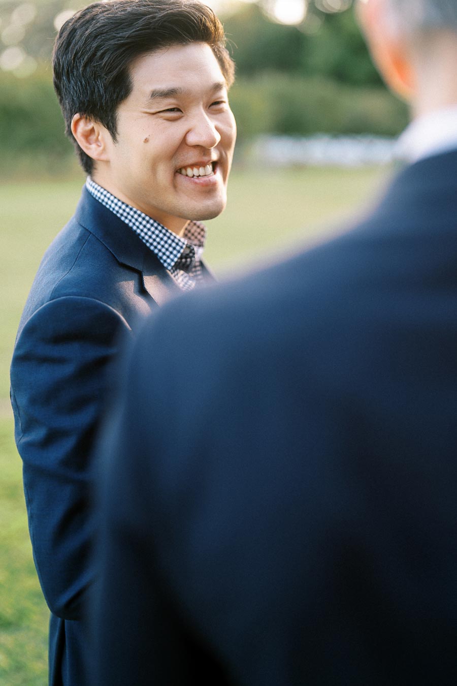A smiling man in a blue suit converses outdoors, with blurred greenery in the background, promoting positive engagement and professional attire.