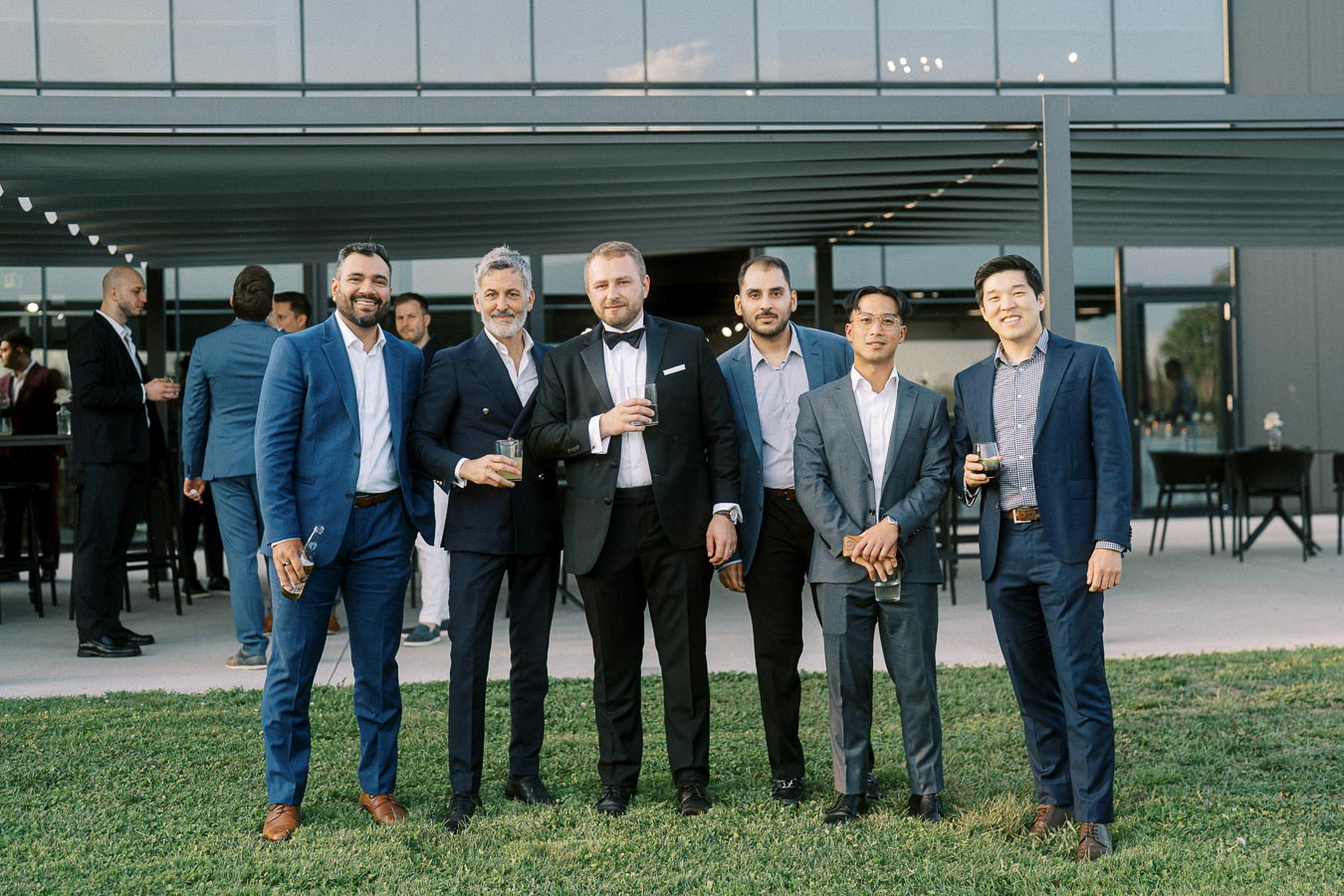 Group of six men dressed in suits standing together outdoors at a business event or formal gathering.