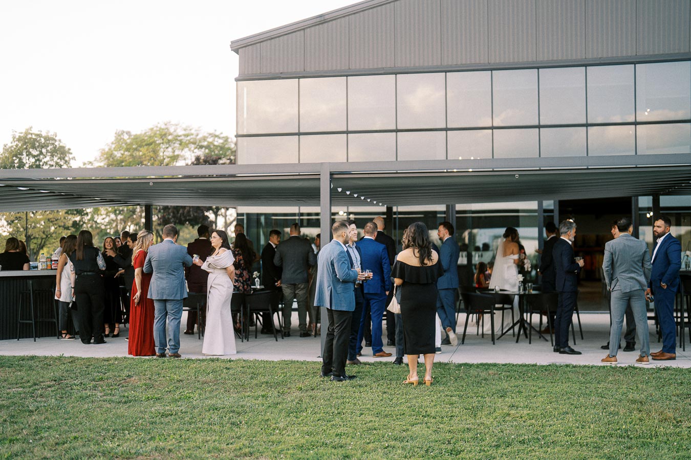 A group of people in formal attire mingling at an outdoor event near a modern building.
