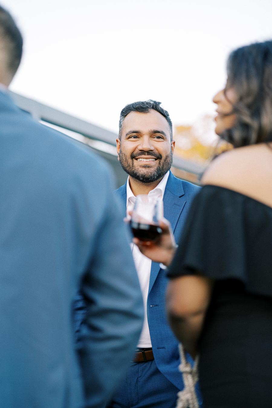 Smiling man in a blue suit engaging in conversation at an outdoor social event.