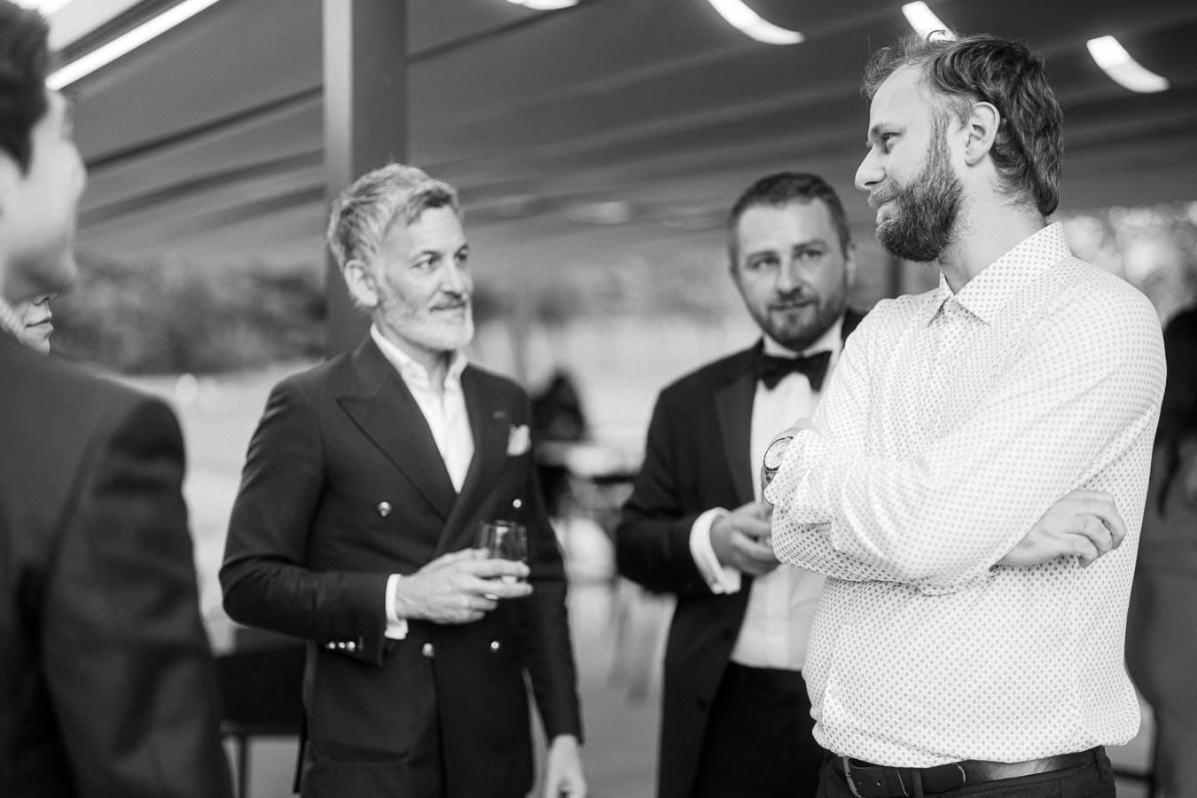 Black and white photo of four men in a formal gathering, socializing and engaged in conversation, with two of them holding beverages.