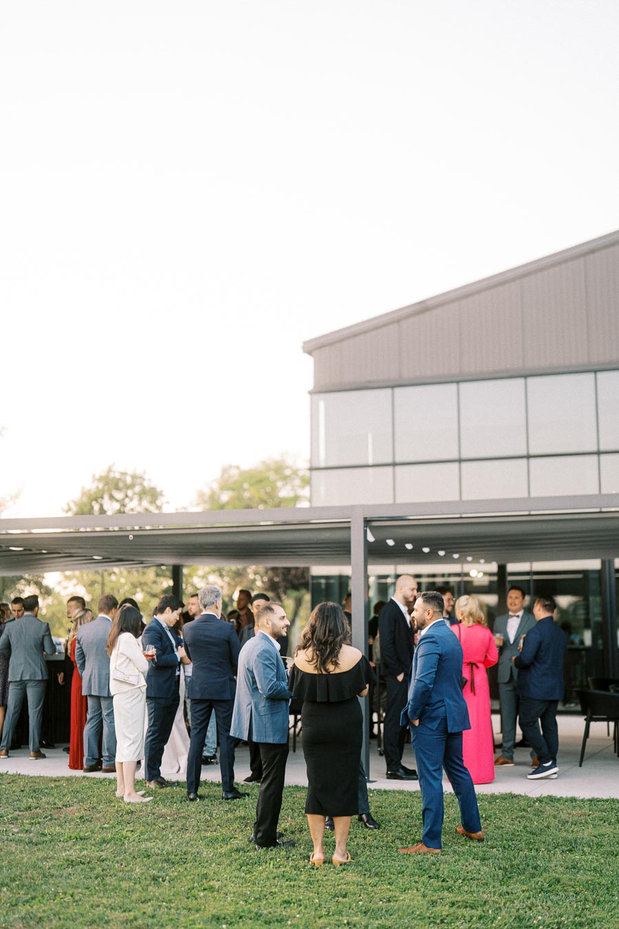 Group of people socializing at an outdoor event with modern architecture in the background, showcasing formal attire and lively conversation.