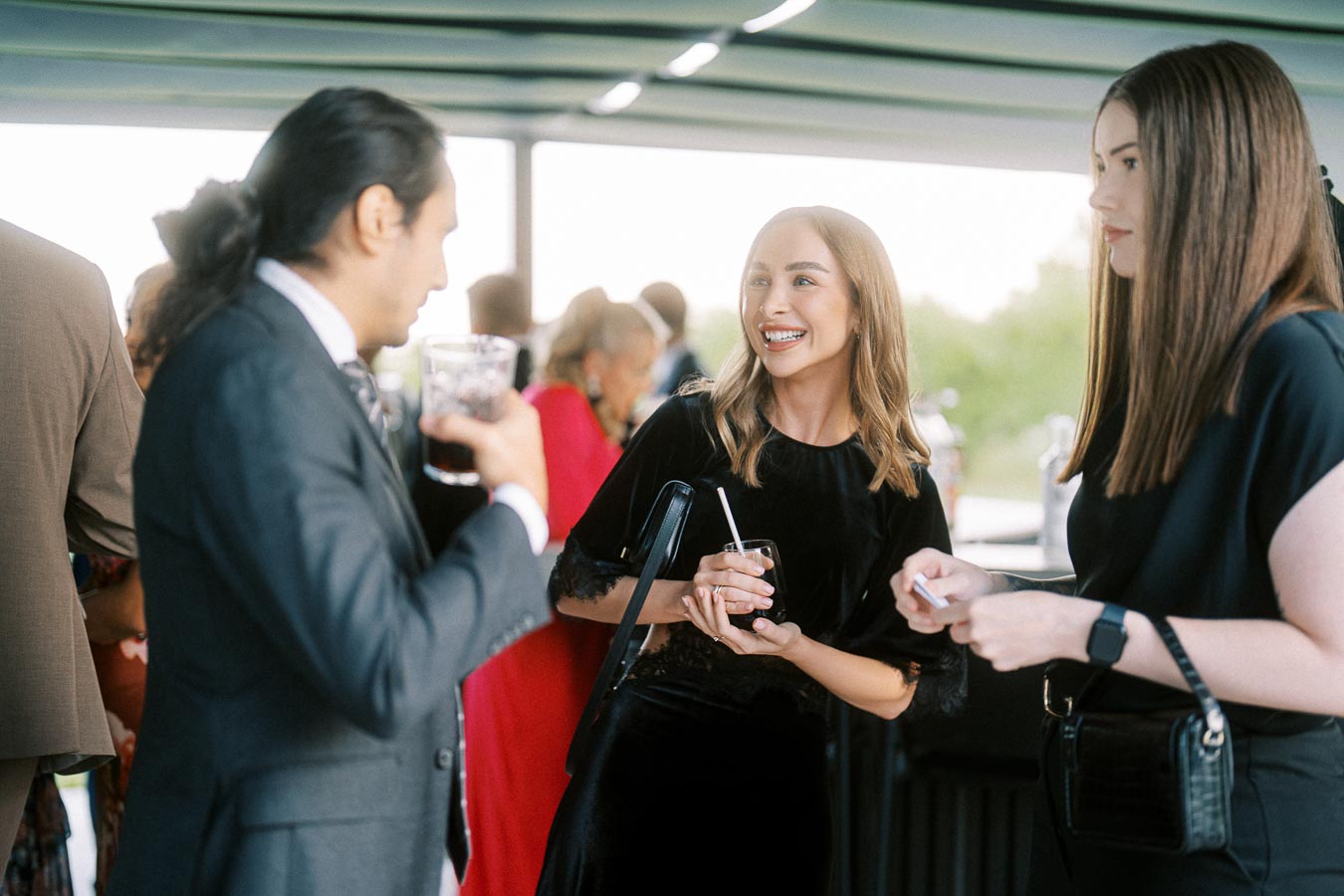 A group of people in formal attire socializing and holding drinks at a lively event.