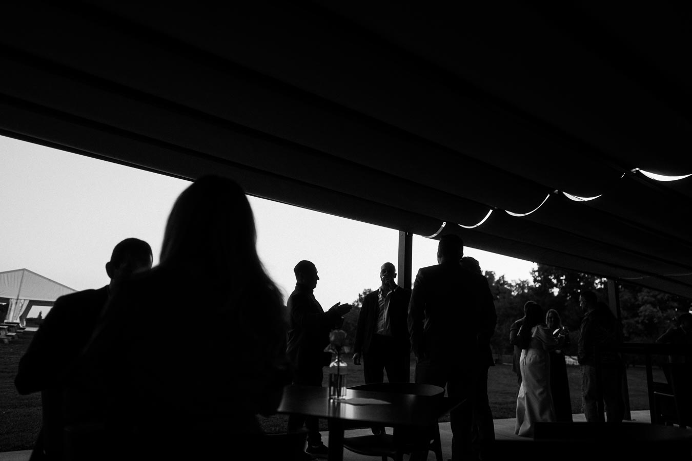 Silhouetted figures gathered under a pavilion during dusk, capturing a serene outdoor gathering with conversations in focus.