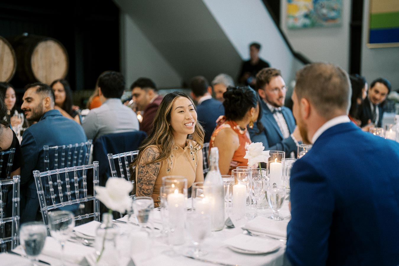 A group of elegantly dressed guests enjoying a candlelit dinner at a formal event, with clear chairs and decorative vases, creating a sophisticated atmosphere.