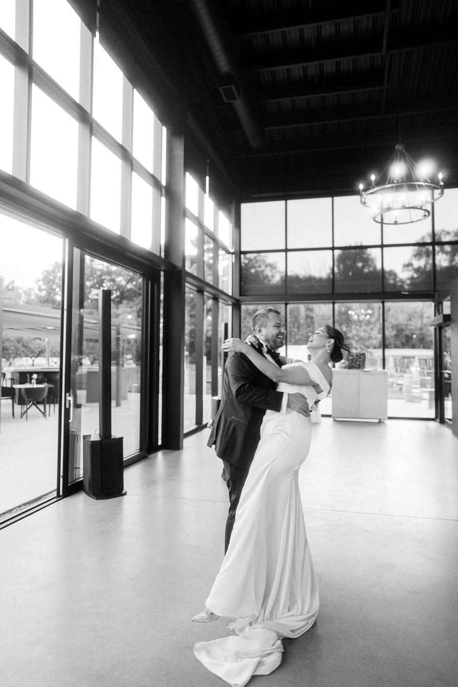 A bride and groom share a joyful dance in an elegant, modern venue with large windows, creating a romantic and intimate wedding atmosphere.