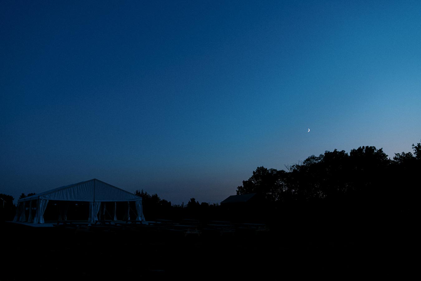 Tent under a twilight sky with a crescent moon and silhouette of trees.