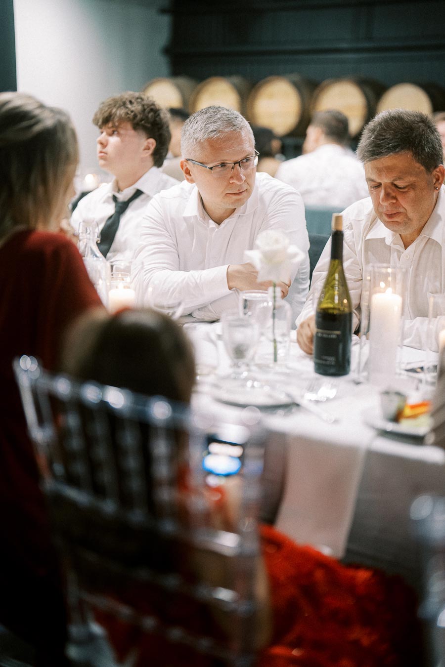 Adults and child gathered around an elegantly set dinner table with wine bottles and candles, engaging in conversation at a formal event.