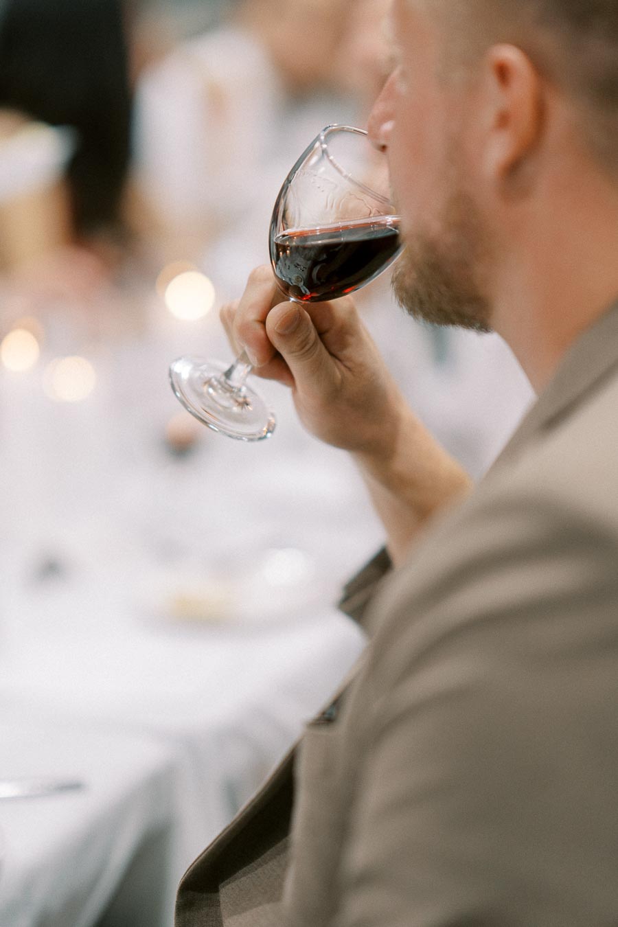 Man sipping red wine at a formal dinner event, close-up shot.