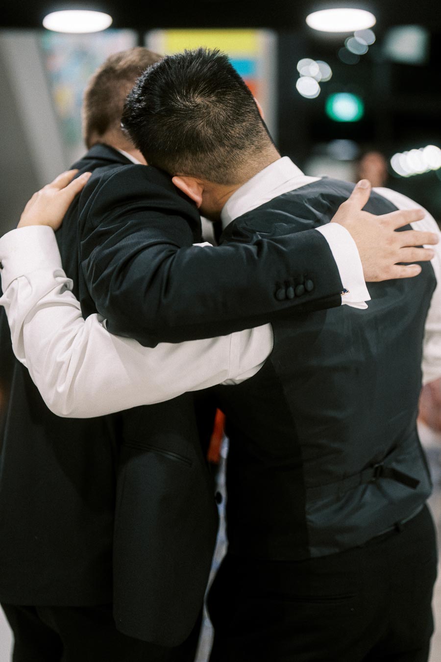 Two men in formal attire embracing warmly at an indoor event, symbolizing friendship and support.