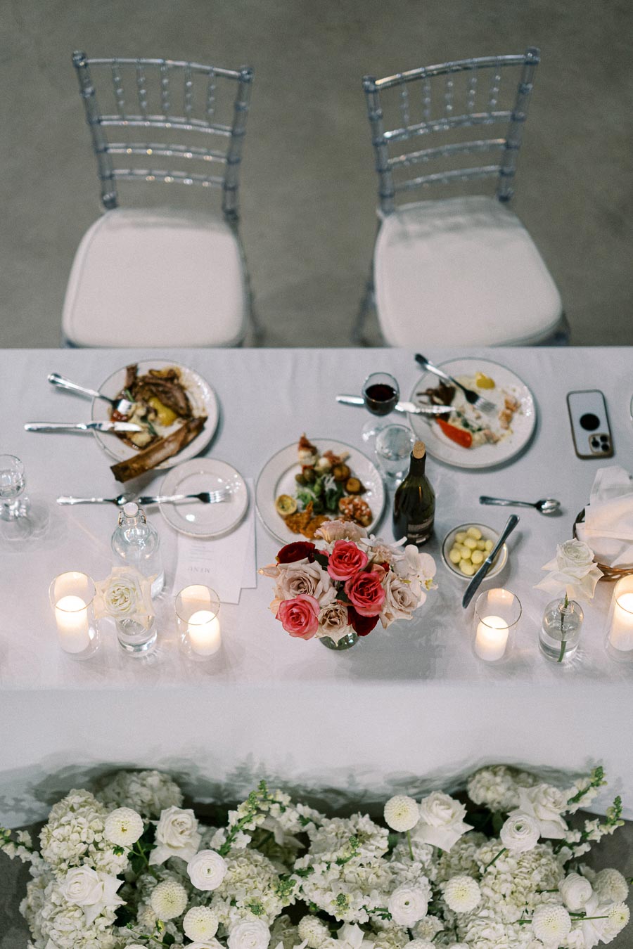 Wedding reception table setting with elegant floral centerpiece, romantic candlelight, and gourmet dining plates, viewed from above.