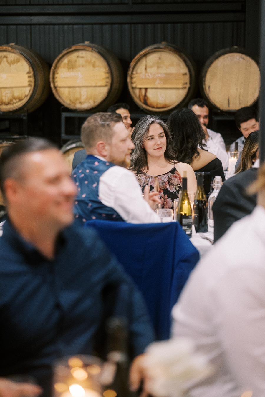 People enjoying a social gathering at a venue with wooden barrels in the background, featuring a warmly lit atmosphere.