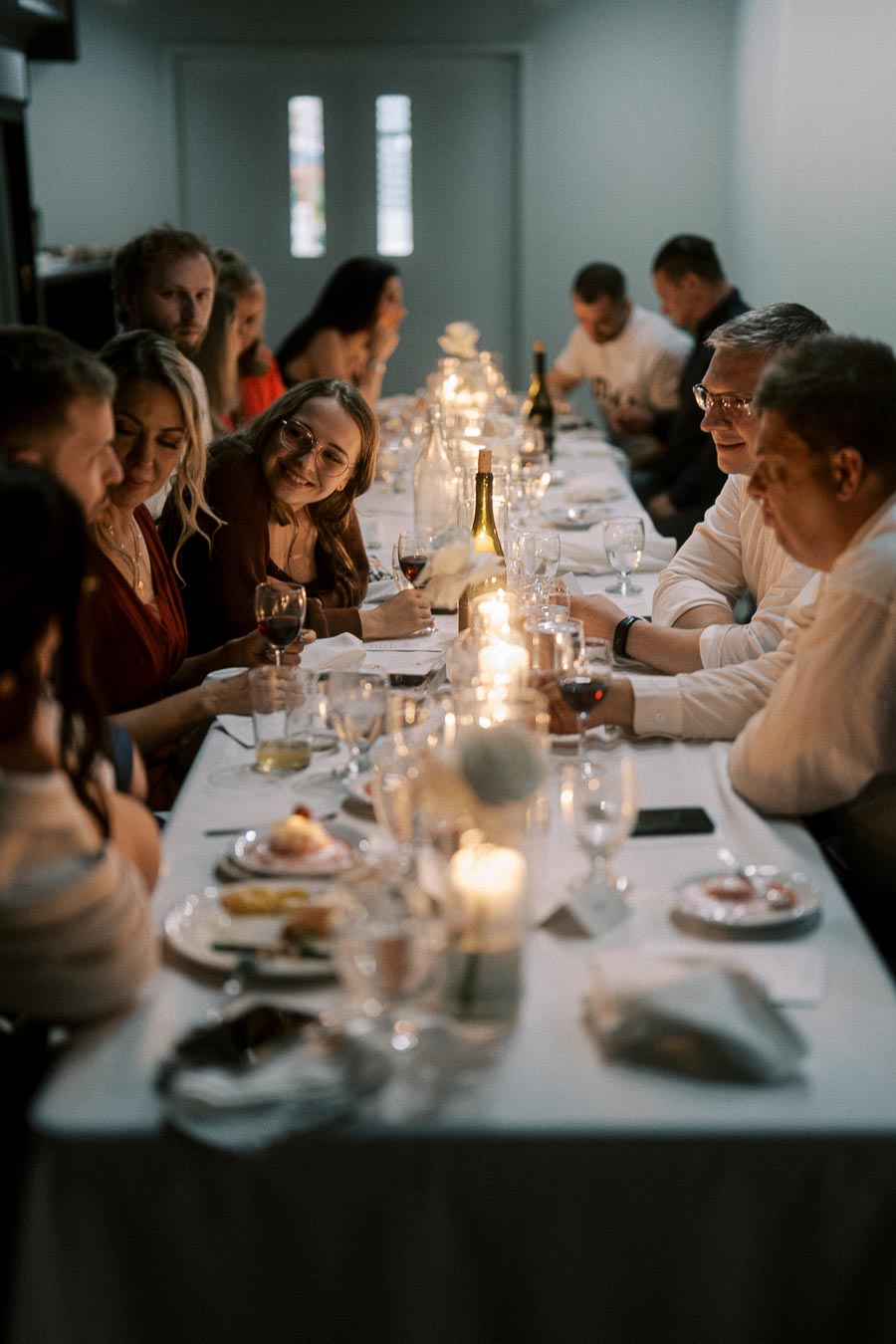 Group of people enjoying a cozy dinner party, seated around a warmly lit table with candles and wine glasses, engaging in lively conversation.
