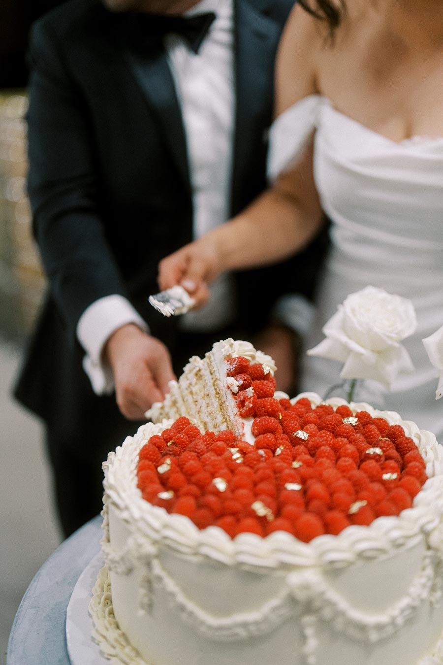 A bride and groom cutting a wedding cake adorned with raspberries and white icing, capturing a celebratory moment at their reception.