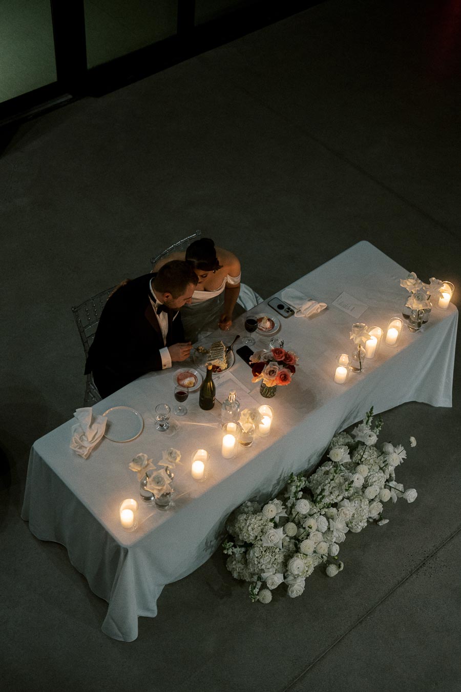 Aerial view of an elegant wedding reception table with a couple seated. The table is adorned with candles, flowers, and a cake, creating a romantic ambiance.