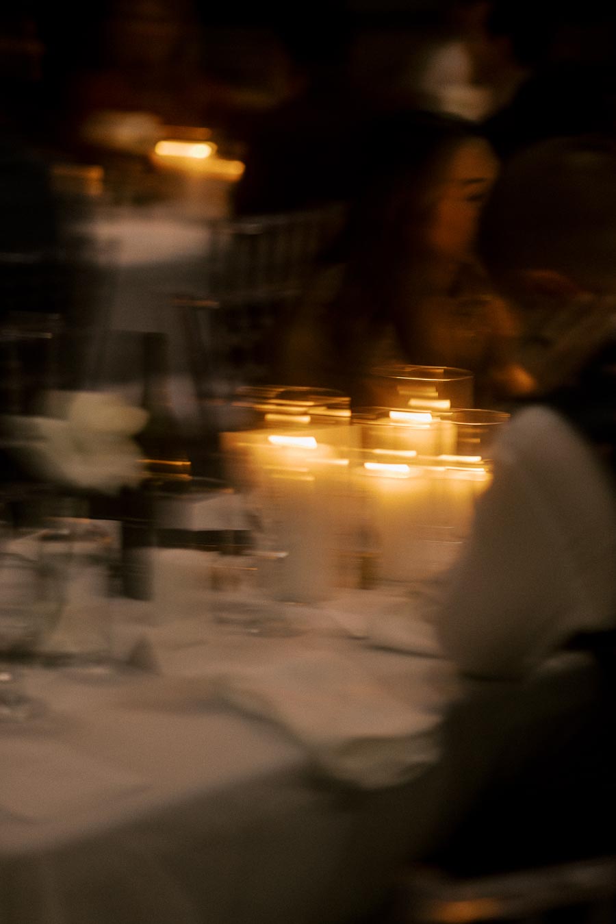 A beautifully blurred image of a candlelit dinner table setting, featuring glowing candles, elegant tableware, and the soft ambiance of a warm, intimate gathering.