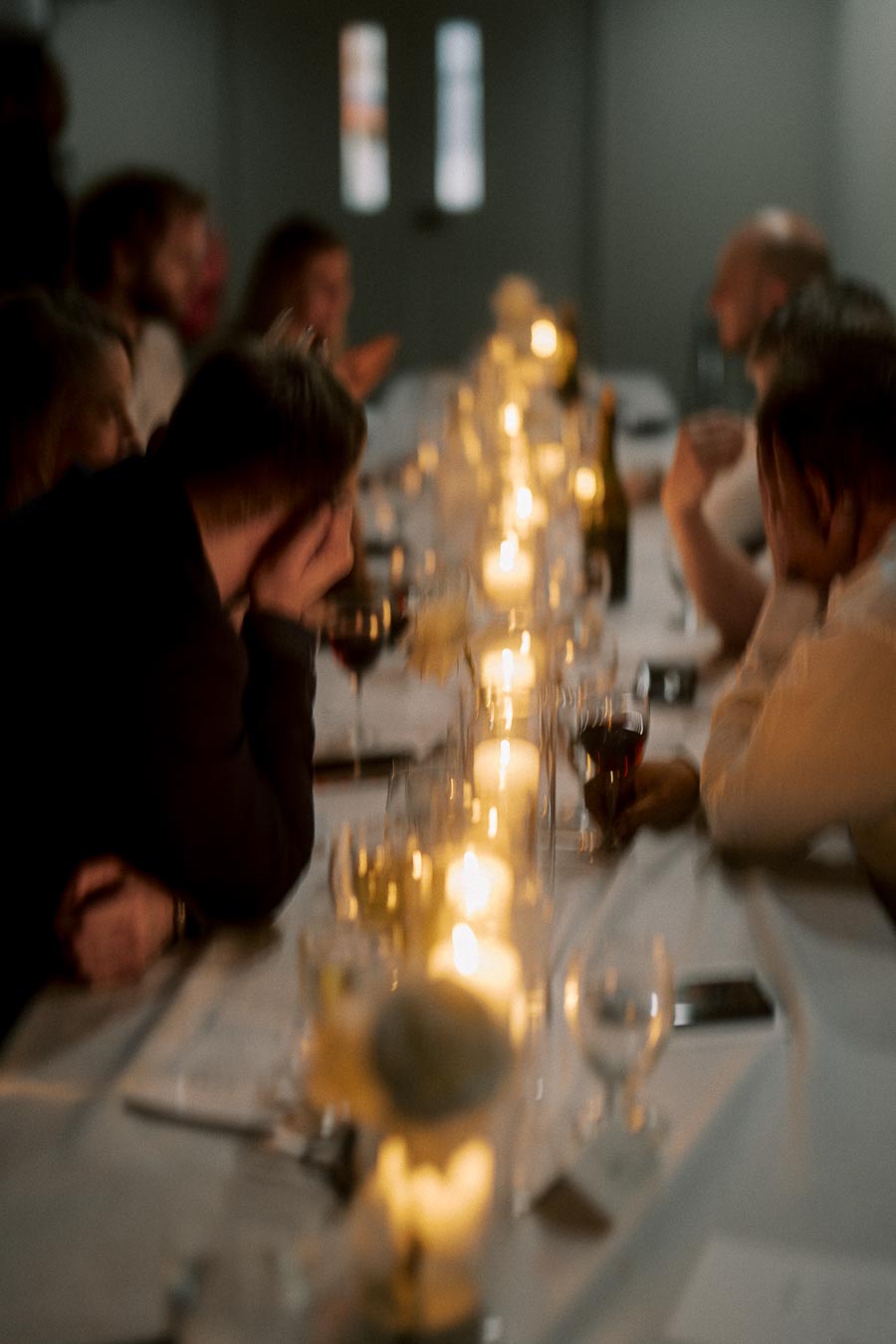 A softly focused image of a dimly lit dinner party, featuring a long table adorned with glowing candles and people engaged in conversation, creating a warm, intimate atmosphere.