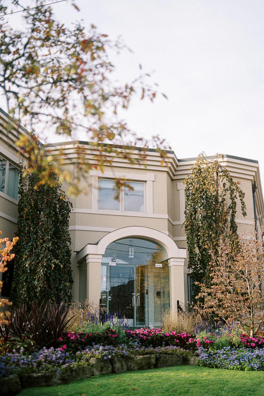 Elegant building entrance with glass doors surrounded by lush gardens and colorful flowers in a tranquil setting