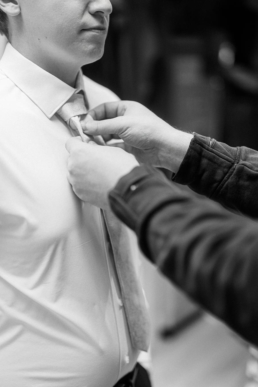 A person adjusting a necktie on someone wearing a dress shirt, showcasing attention to detail in professional attire. Black