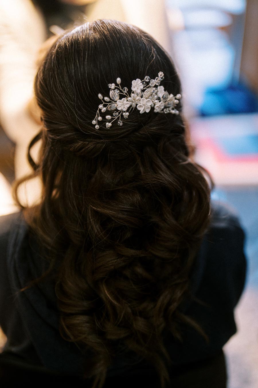 Brunette hair styled in elegant curls with a delicate floral hairpiece adorned with pearls and crystals.