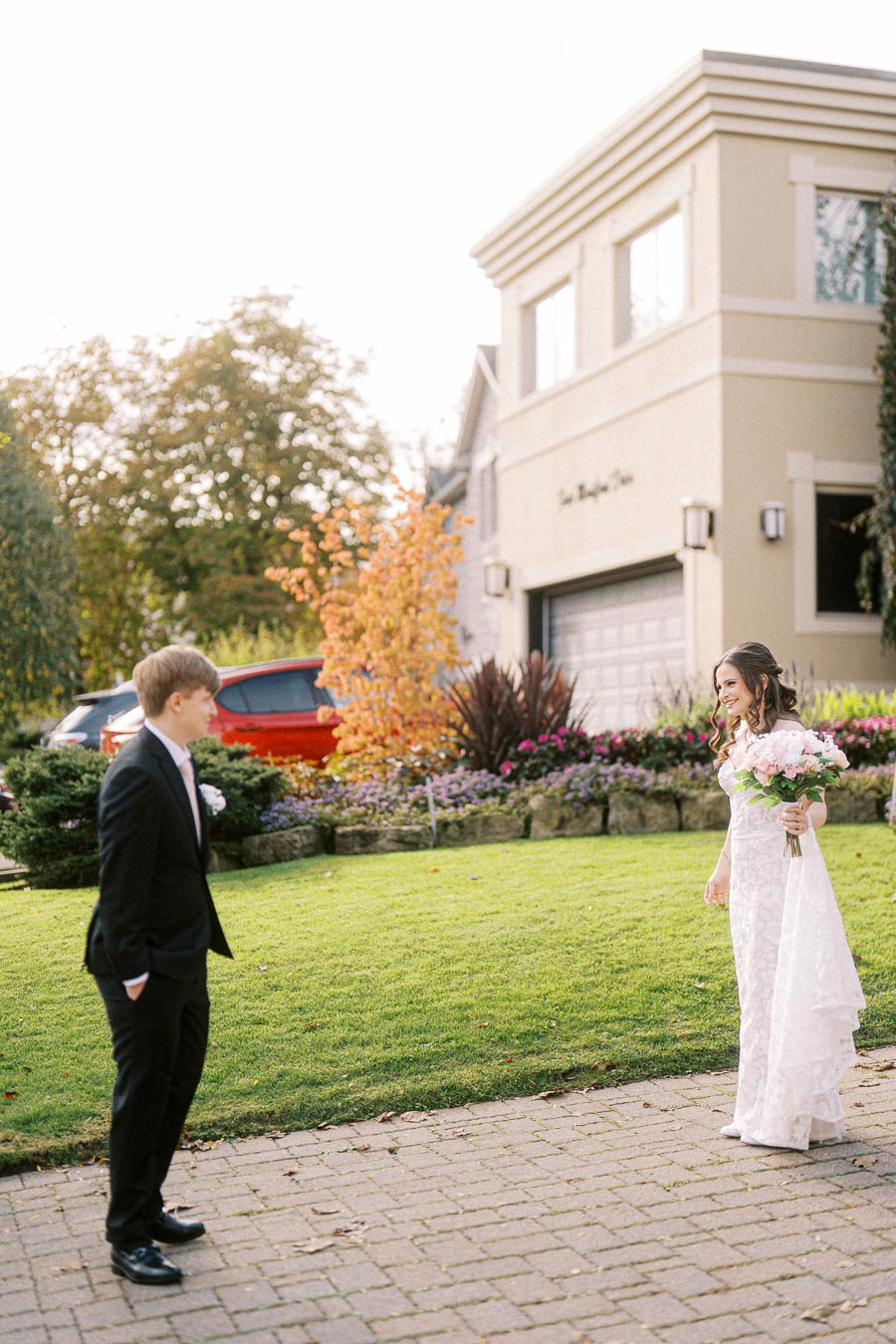 A bride and groom sharing a special moment outside a house with a beautifully landscaped garden, featuring autumn foliage