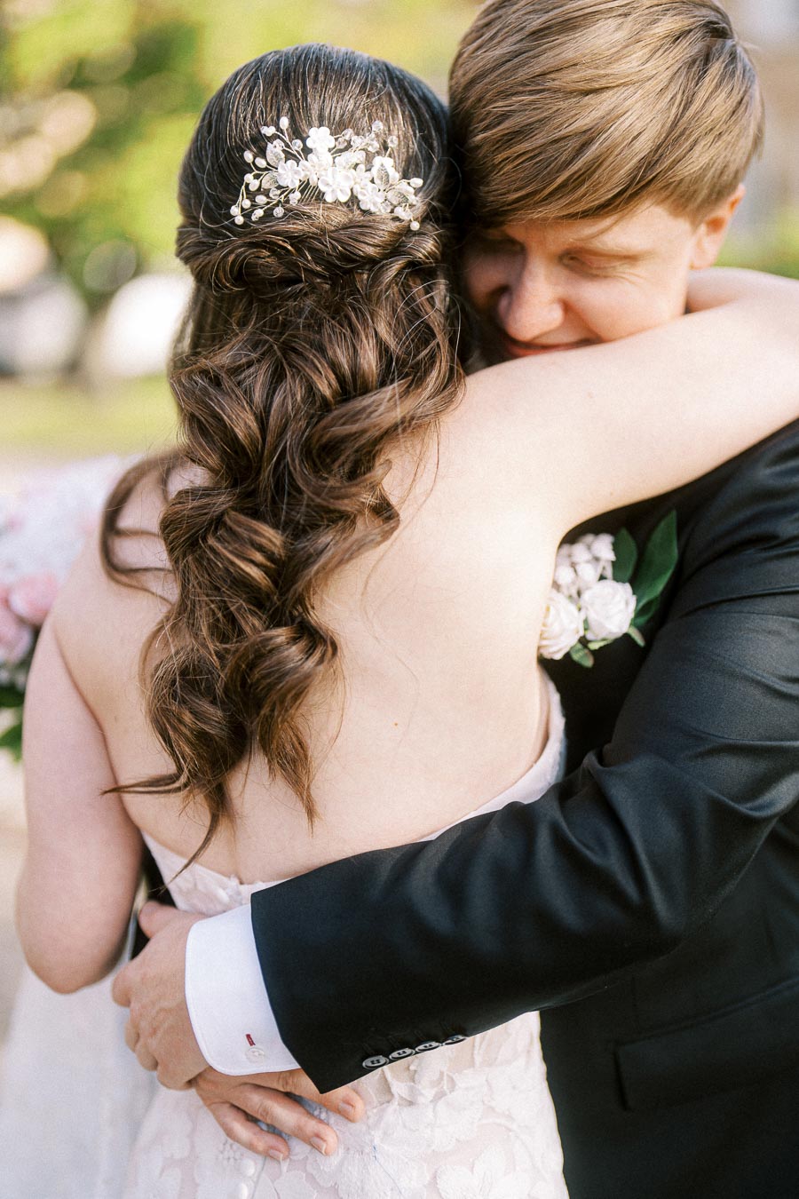 A bride and groom share an intimate embrace on their wedding day, with the bride's intricately styled hair adorned with a
