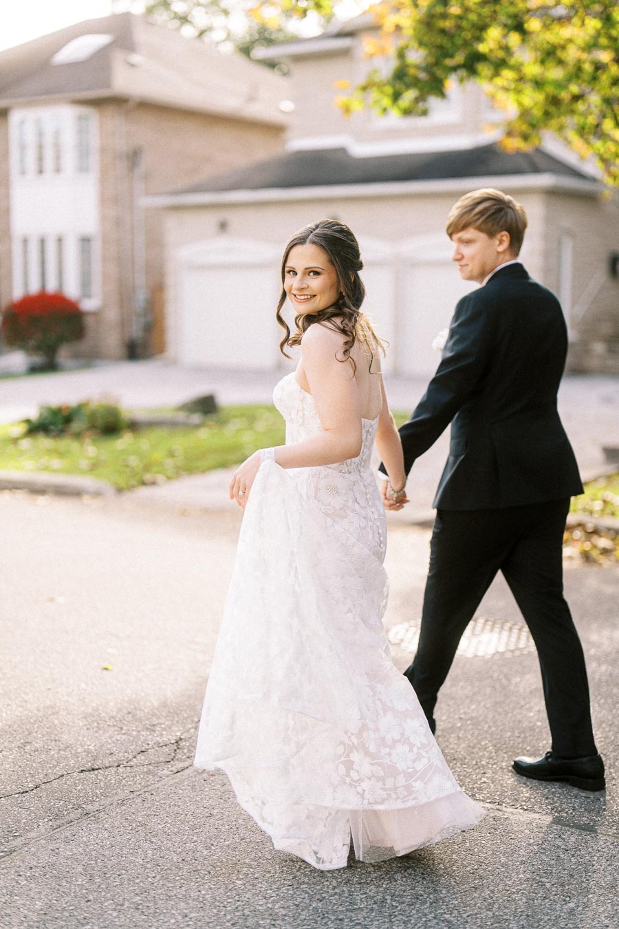 Smiling bride in a beautiful lace wedding dress walking hand in hand with her groom in a black suit, on a sunny day in a
