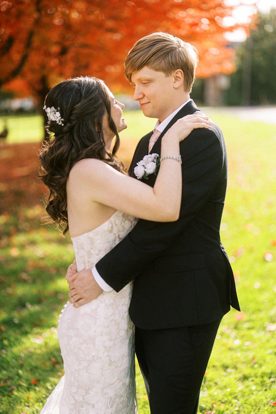 A bride and groom embrace on their wedding day with vibrant autumn leaves in the background, capturing a romantic moment in