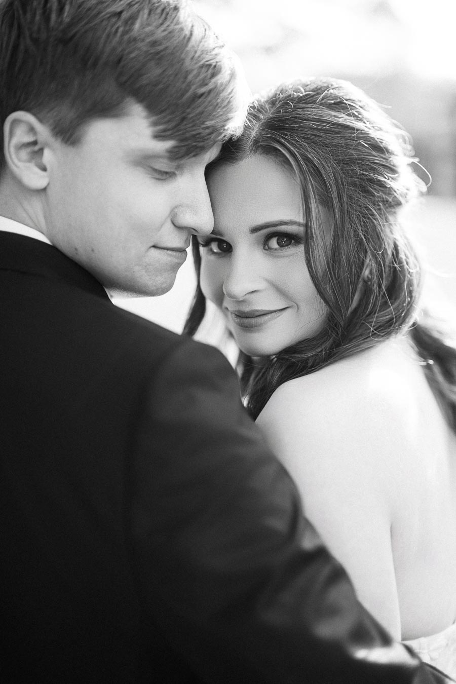 A black-and-white photo of a couple embracing, with the woman looking at the camera and smiling while the man has his eyes