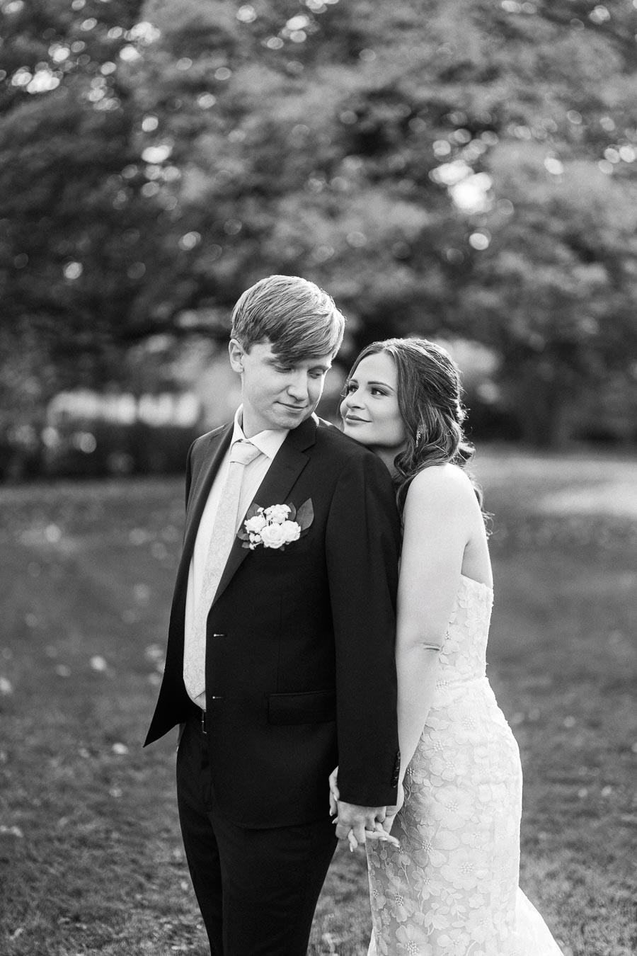 Black and white photo of a couple on their wedding day, with the bride affectionately leaning on the groom's back in a