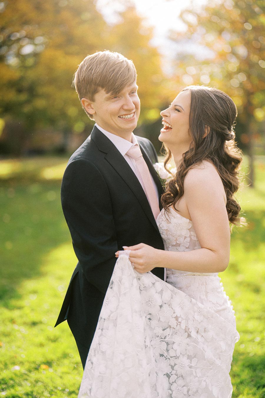 A joyous couple celebrating their wedding day in a sunlit garden, with the bride in a lace gown and the groom in a dark