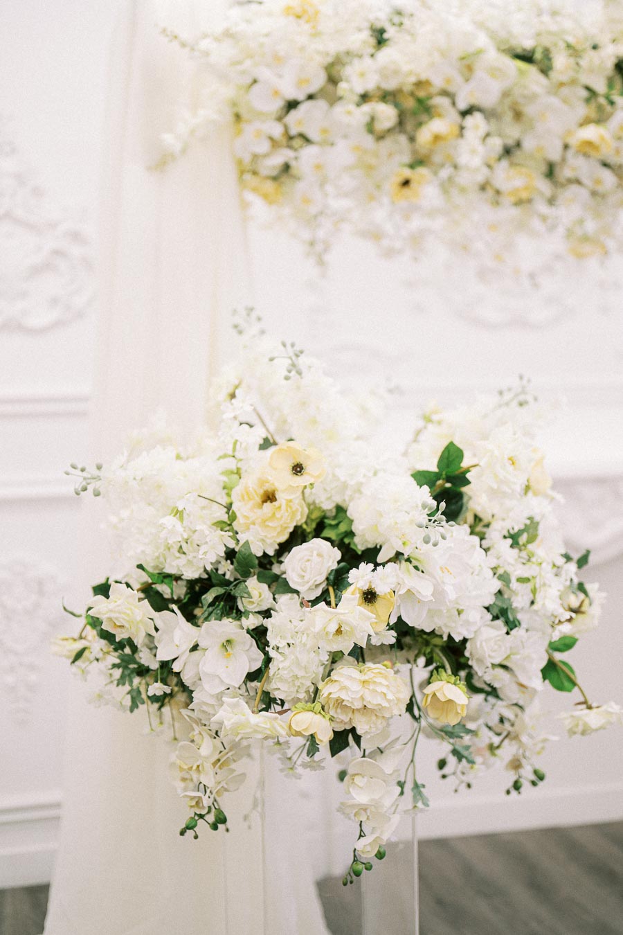 Elegant floral arrangement featuring white and pale yellow flowers with greenery, set against a soft, textured white