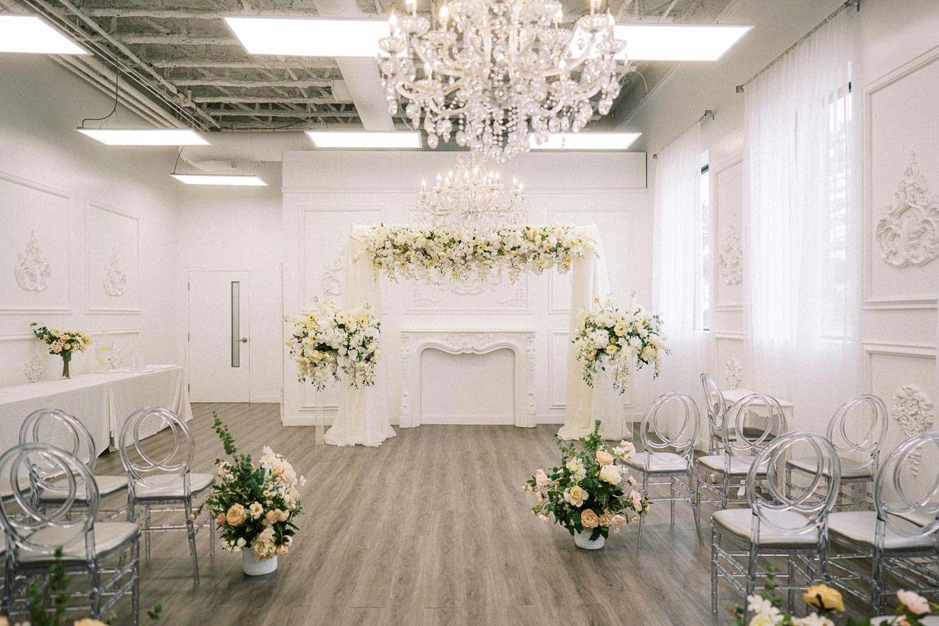 Elegant wedding ceremony venue with white walls, crystal chandeliers, and floral arch decorated with white and yellow