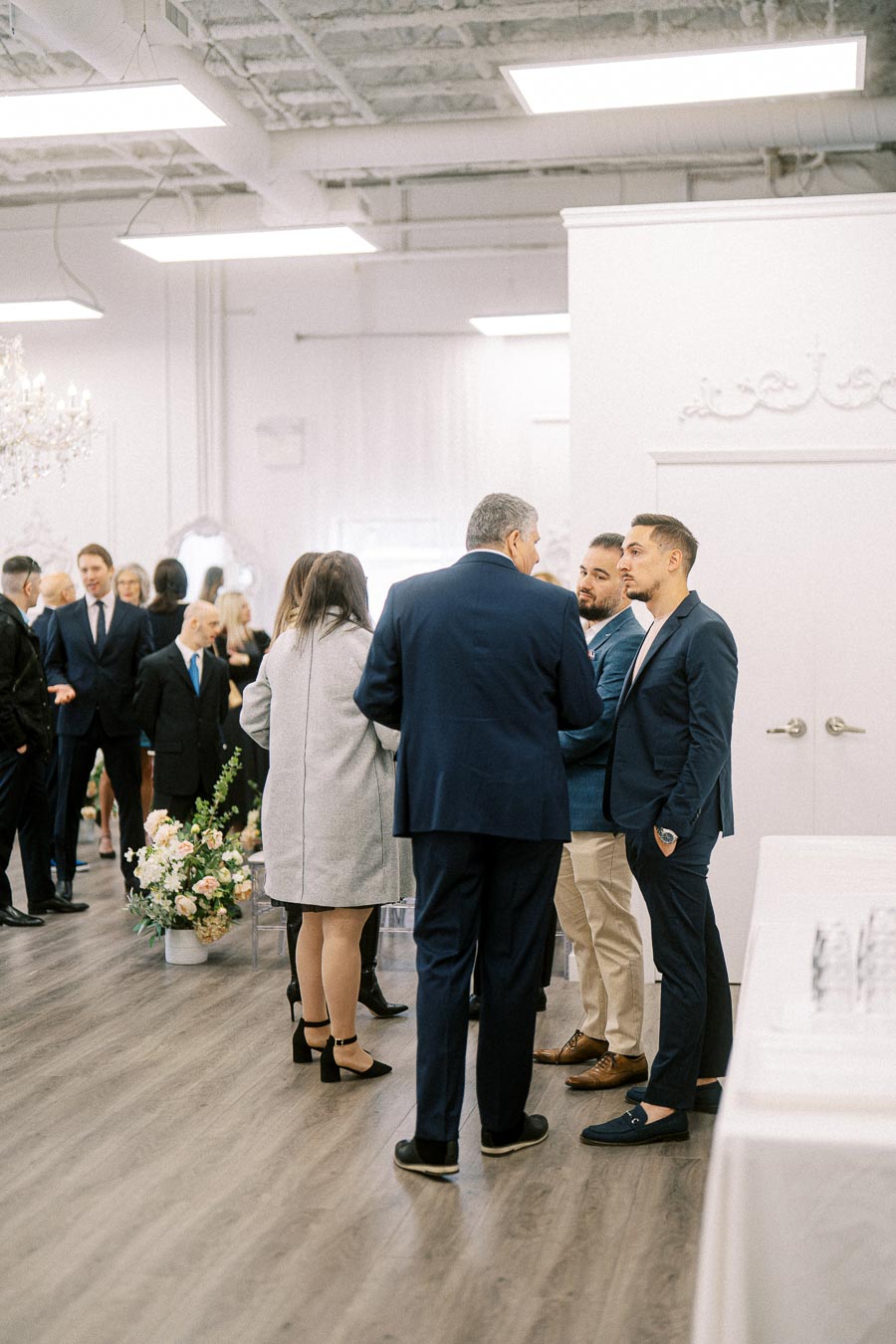 Formal gathering in a modern venue with guests engaging in conversation, dressed in business attire, surrounded by elegant