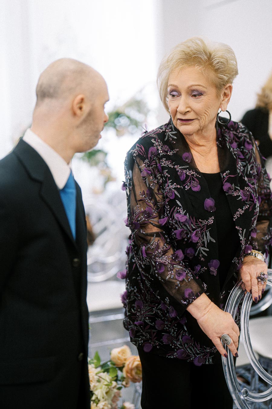 A woman wearing a floral embroidered jacket engages in conversation at an indoor event.