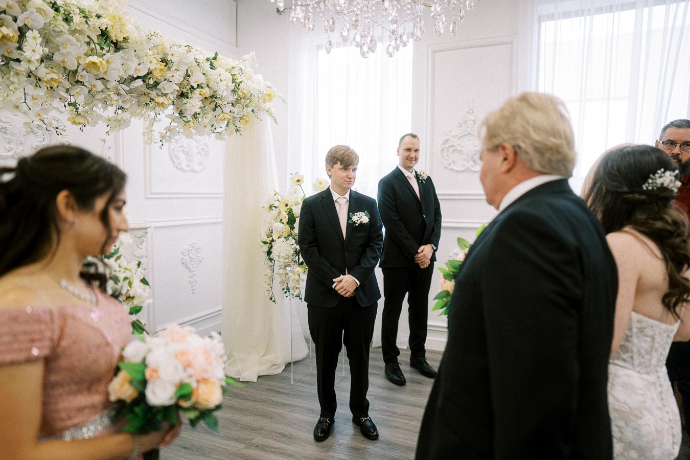 Groom standing at the altar in an elegant, flower-adorned wedding ceremony room, anticipating the entrance of the bride,