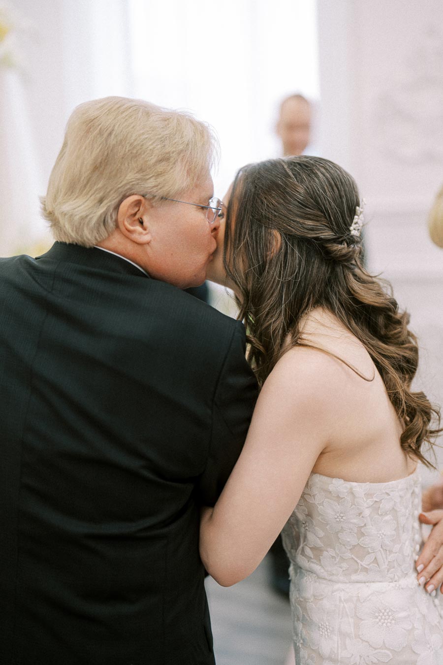A father giving his daughter a loving kiss on her wedding day, capturing a tender moment as she wears an elegant white gown