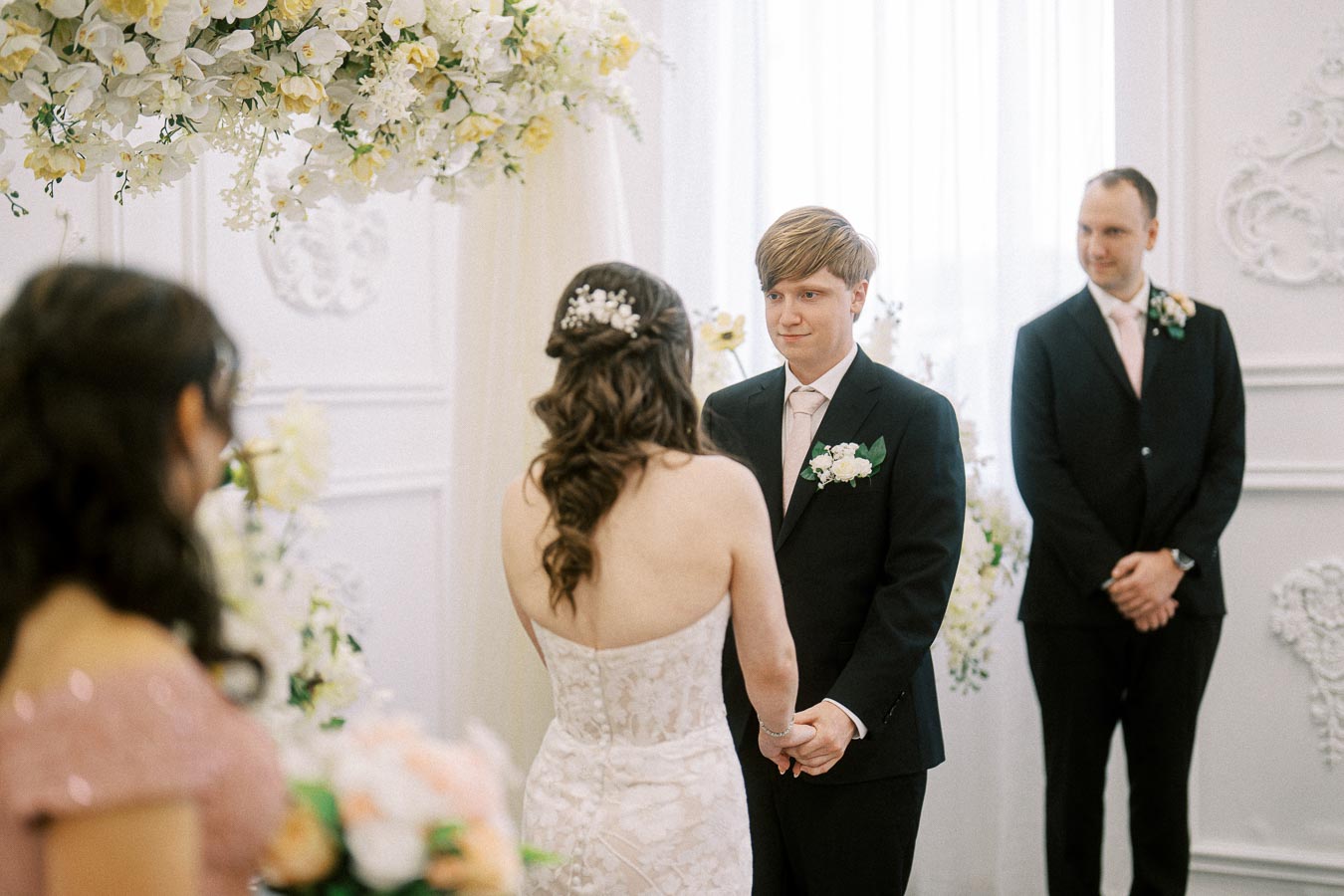 A bride and groom holding hands during a wedding ceremony in an elegantly decorated venue with floral arrangements and a