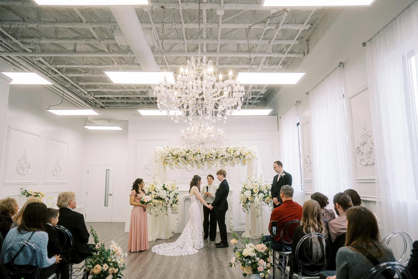 A bride and groom exchanging vows in a beautifully decorated modern wedding venue, surrounded by floral arrangements and