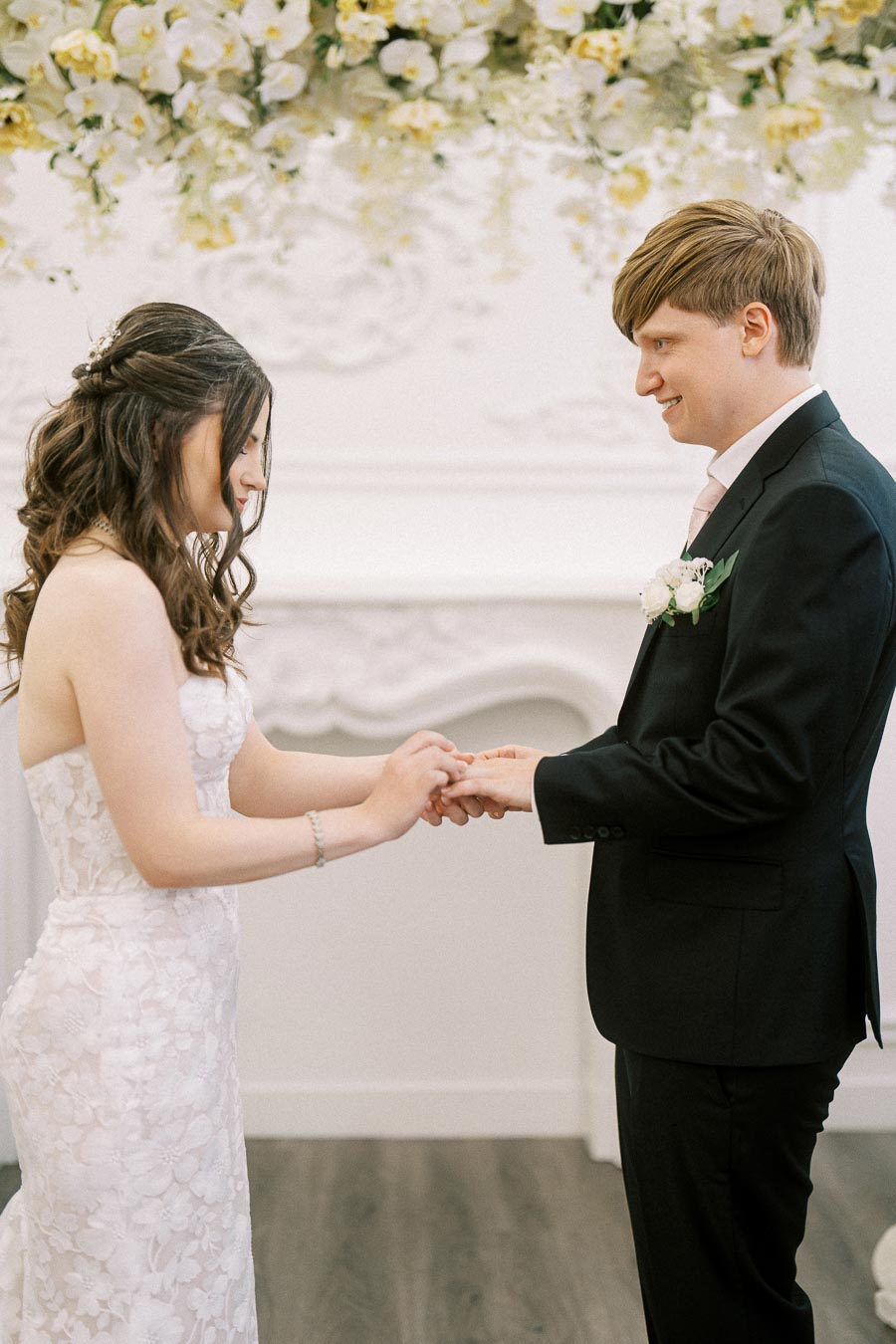Bride and groom exchanging rings during elegant indoor wedding ceremony with floral decor.