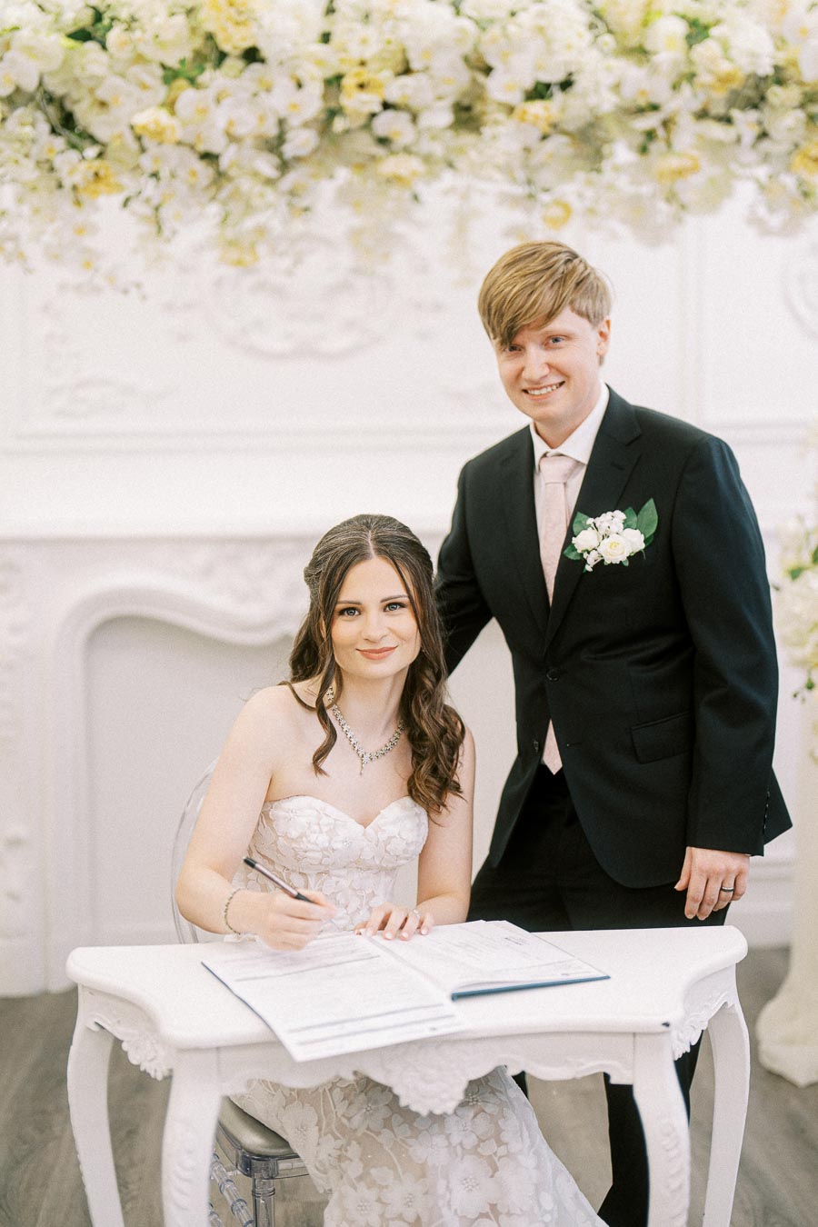 Bride and groom smiling as they sign the marriage certificate at a beautifully decorated wedding venue, showcasing elegant