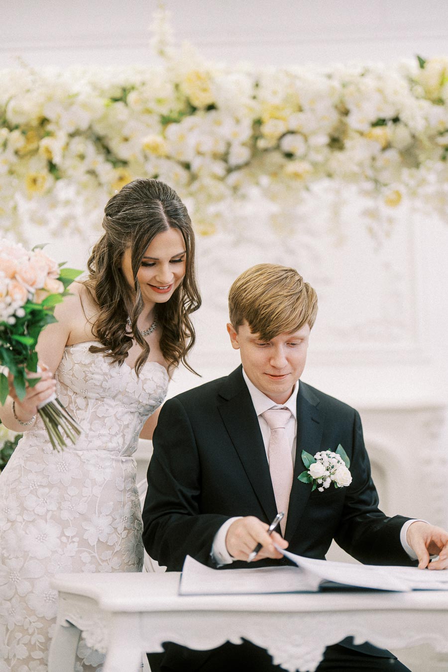 Bride and groom signing wedding documents at a beautifully decorated ceremony, with floral arrangements in the background.