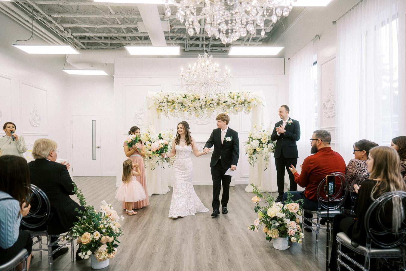Wedding ceremony in a beautifully decorated venue with a bride and groom walking down the aisle, surrounded by guests