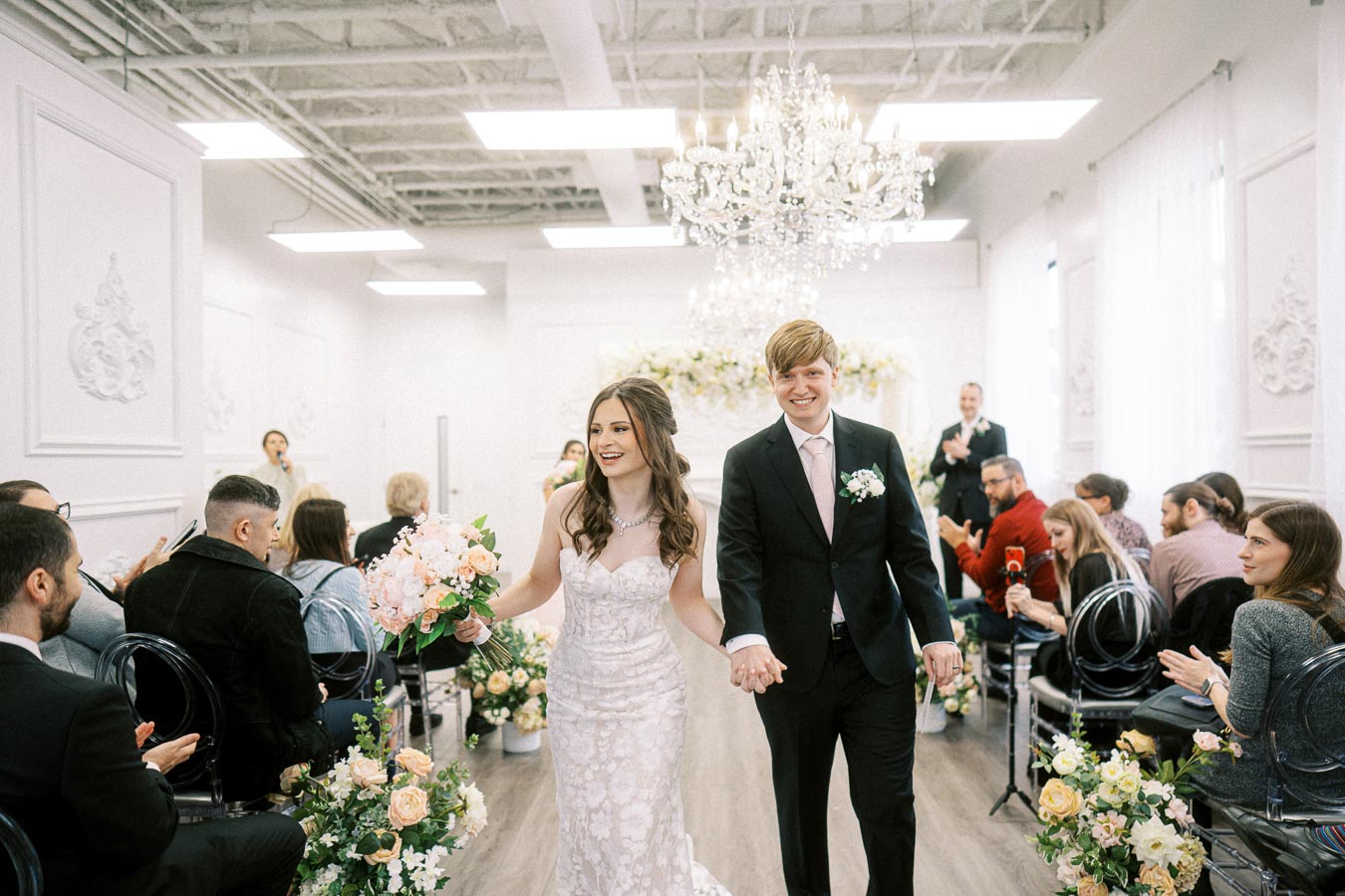A happy couple walking down the aisle after their wedding ceremony, surrounded by guests applauding in a beautifully