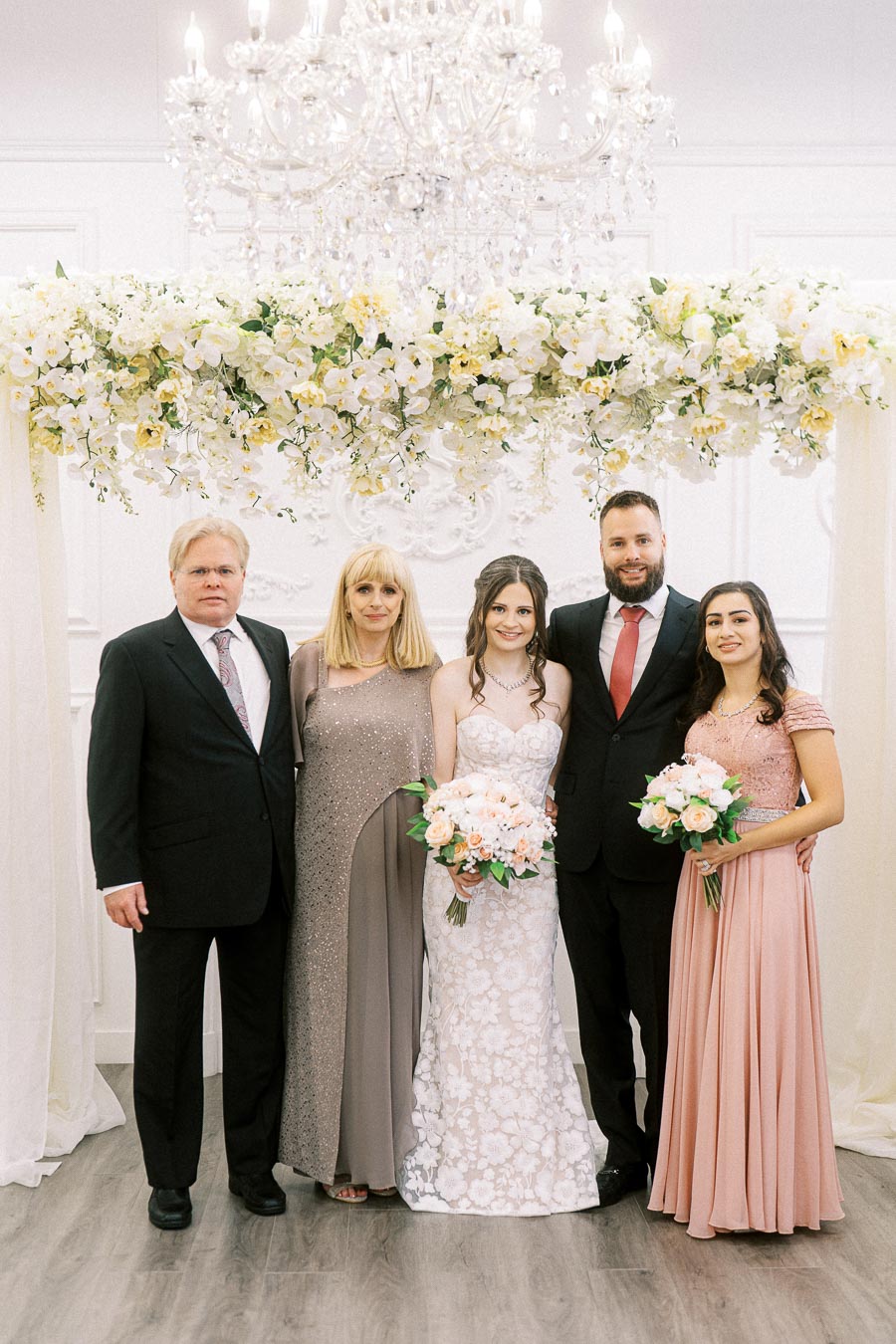 A wedding ceremony capturing a joyful group portrait of a bride in an elegant white gown holding a bouquet, flanked by her