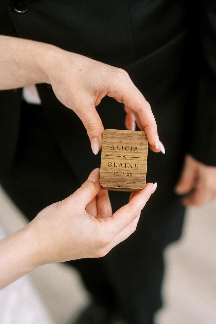 Hands holding a personalized wooden ring box engraved with names and a wedding date, ideal for wedding ceremonies and